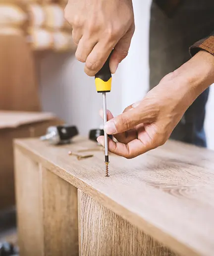 Möbelstück wird mit Hilfe von Schrauben mittels Kreuz-Schraubendreher montiert.